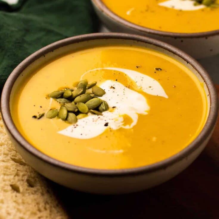 A bowl of creamy pumpkin soup garnished with seeds and a swirl of cream.