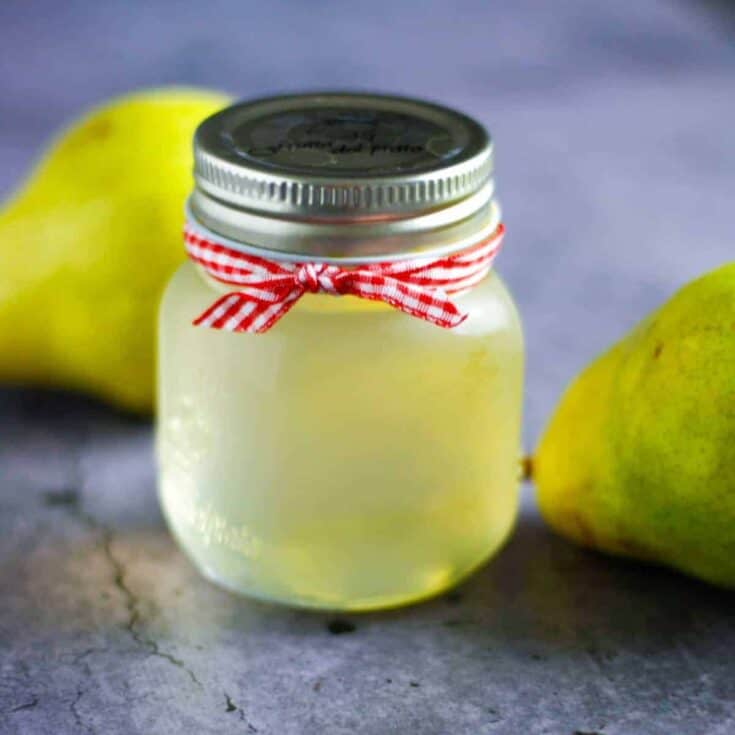 Fresh homemade pear jam in a glass jar with pears in the background.