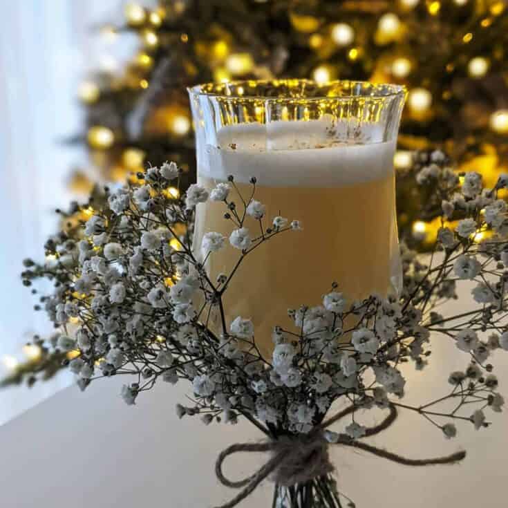 Glass of creamy holiday beverage surrounded by baby's breath flowers with Christmas tree in the背景.
