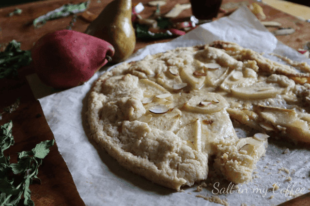 Fresh pear and almond galette on parchment paper with pears and pears in background.