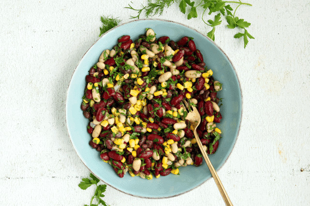 Colorful bean and corn salad in a blue bowl with herbs on a light background.