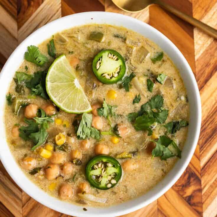 Creamy chickpea and vegetable curry with lime and jalapeño slices in a white bowl.