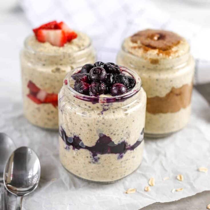 Three layered berry parfaits with strawberries, blueberries, and oats in glass jars.