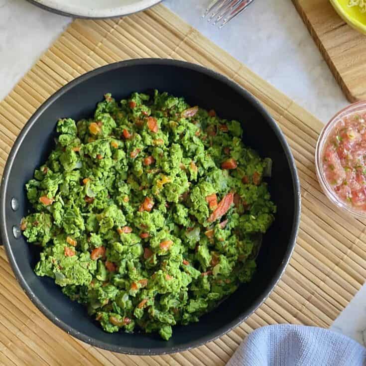 Healthy kale salad with tomatoes and bacon in a black bowl on a wooden mat.