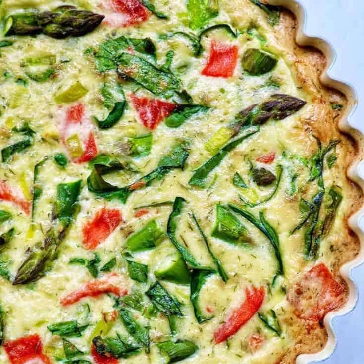 Fresh vegetable quiche with asparagus, tomatoes, and green onions in a baked pastry crust.