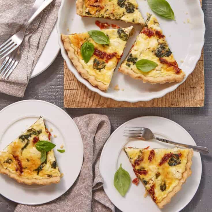 Fresh spinach and cheese vegetarian pizza slices on white plates, rustic table setting.
