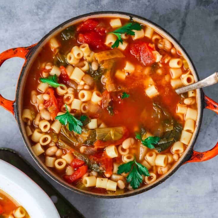 Hearty vegetable minestrone soup in a rustic cast iron pot, fresh herbs and pasta, healthy comfort food.