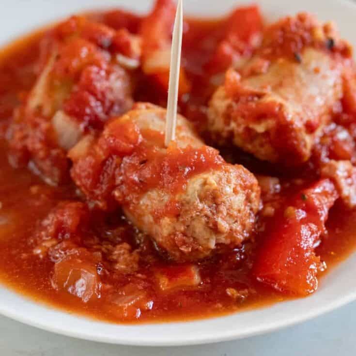 Savory meatballs in tomato sauce served on a white plate.