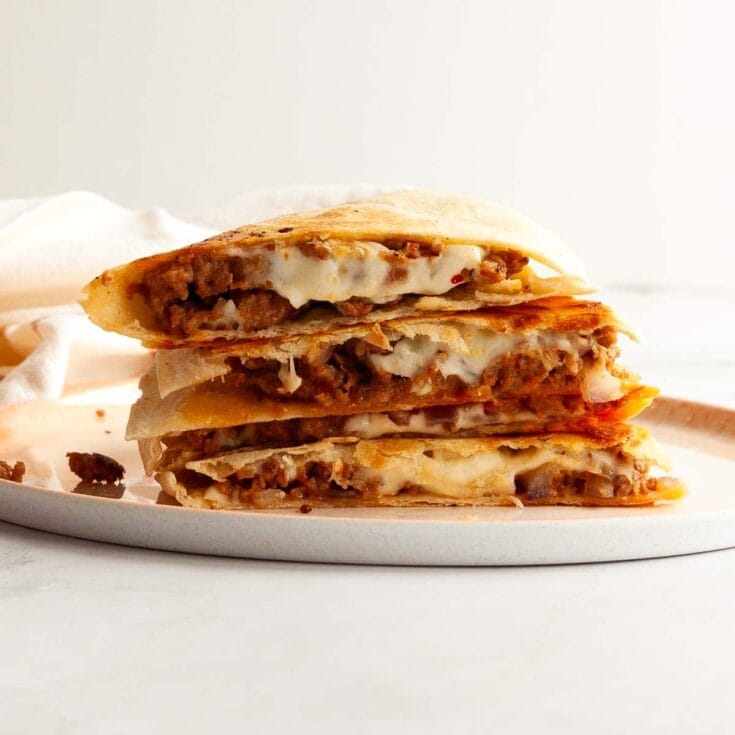 Close-up of a homemade meat and cheese quesadilla sliced in half on a white plate.
