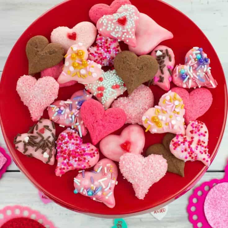 Colorful heart-shaped Valentine's Day cookies with sprinkles in a red bowl.
