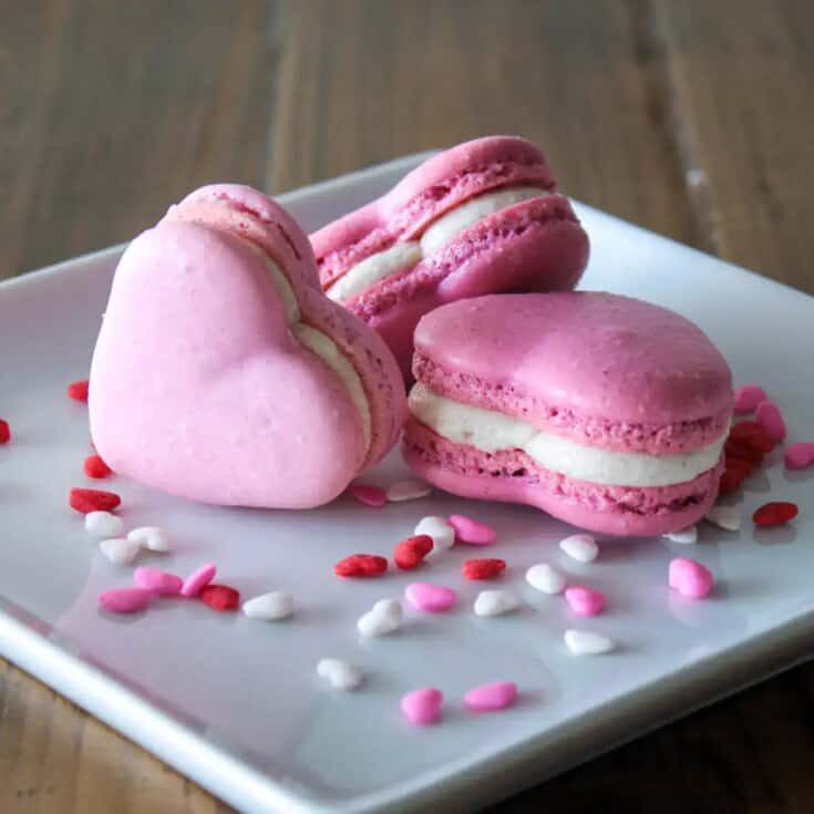 Pink heart-shaped macarons with white filling on a white plate, Valentine's Day dessert.