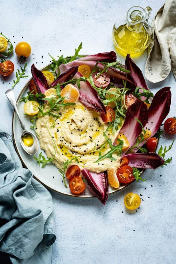 Vibrant salad with hummus, cherry tomatoes, radicchio, and arugula.