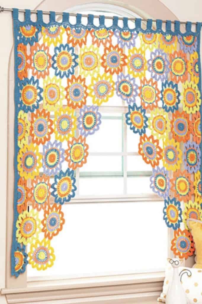 Colorful crochet sunflower window curtain in bright yellow, orange, blue, and purple by The Olive Branch Nest.