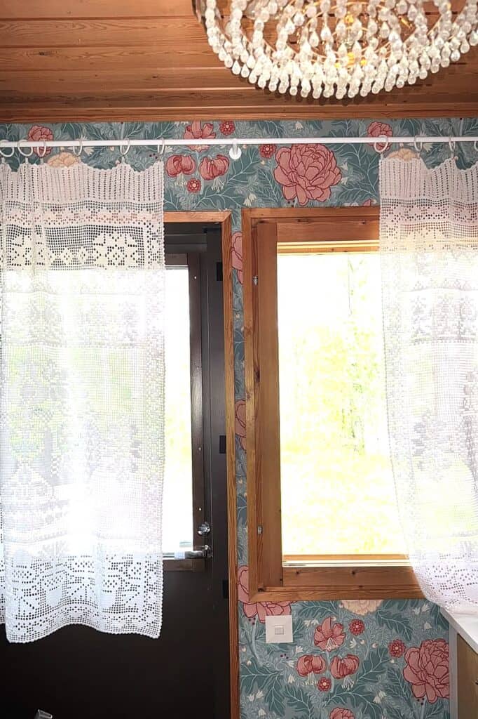 Charming floral wallpaper with lace curtains and wooden window frames.
