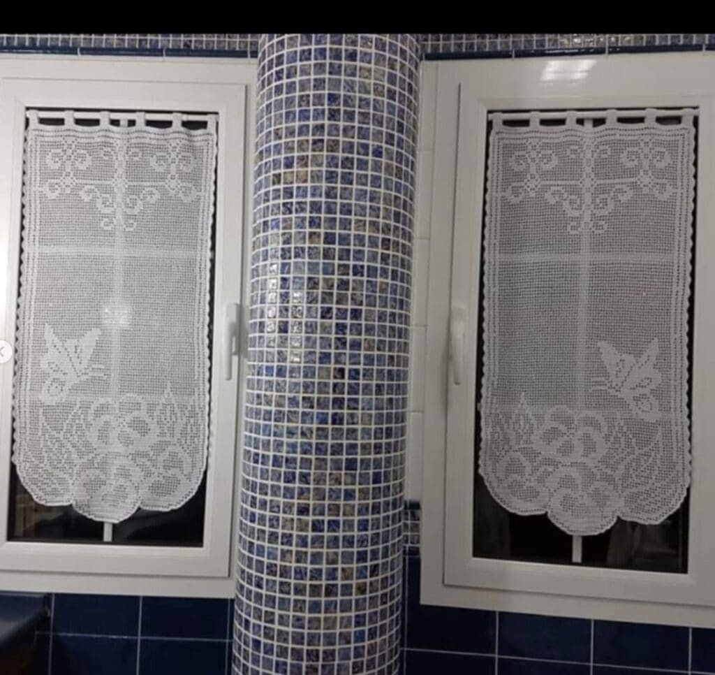 Delicate lace curtains with floral patterns on bathroom window, blue mosaic tiles.