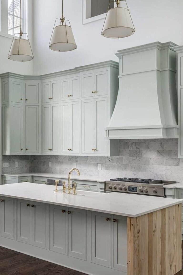 Bright farmhouse kitchen with white cabinetry, marble backsplash, and brass fixtures.