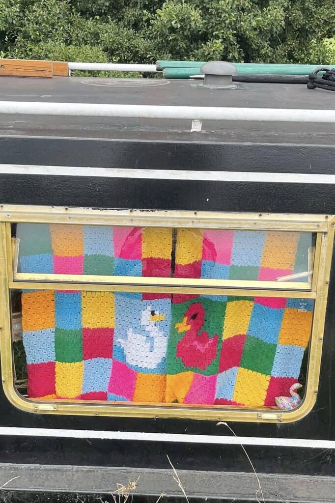 Colorful crocheted blanket with duck and flamingo motifs inside a vintage trailer window.