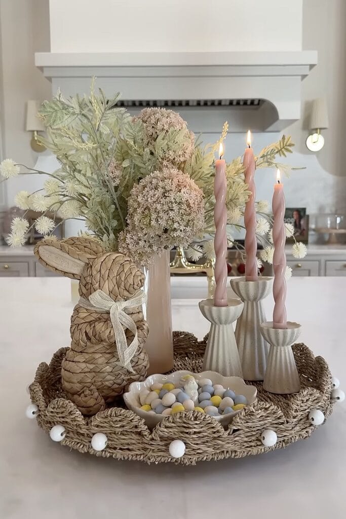 Elegant floral centerpiece with candles and woven bunny decoration.