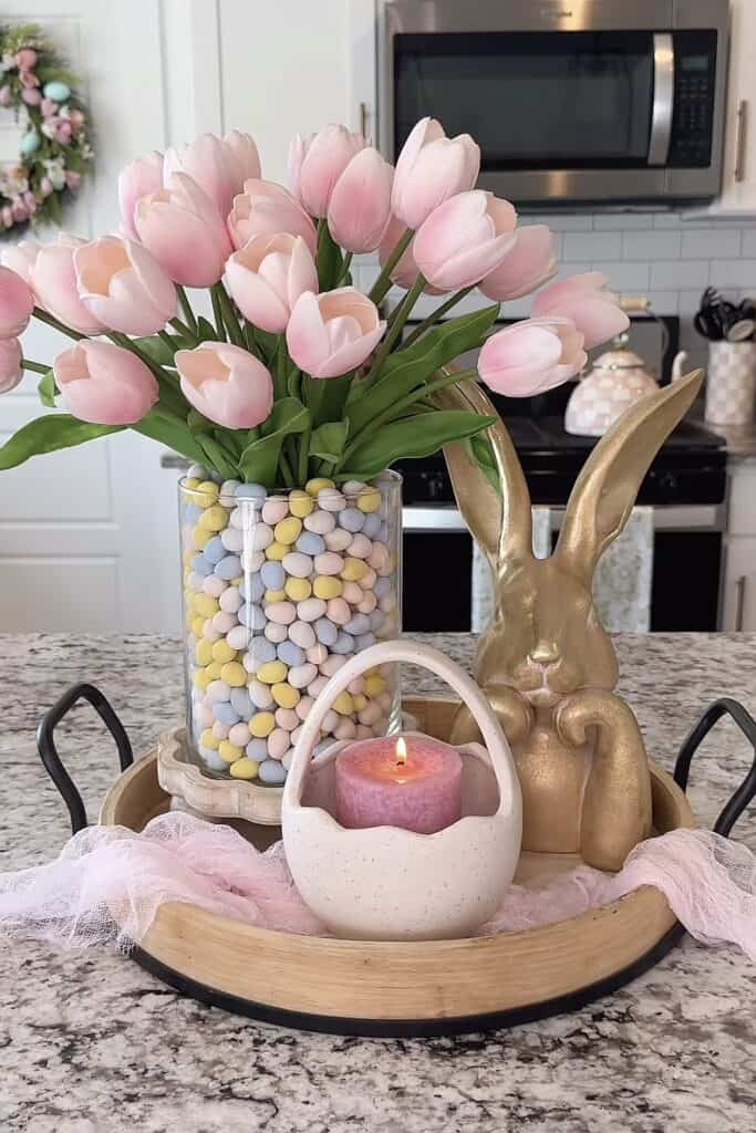 Bright pink tulips in a glass vase with pastel-colored candy-coated eggs and seasonal decorations.