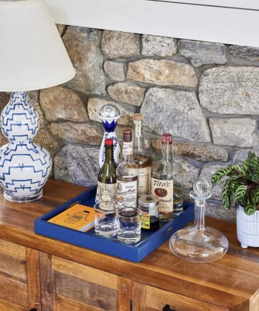 Blue serving tray with alcohol and glasses on wooden table against stone wall.