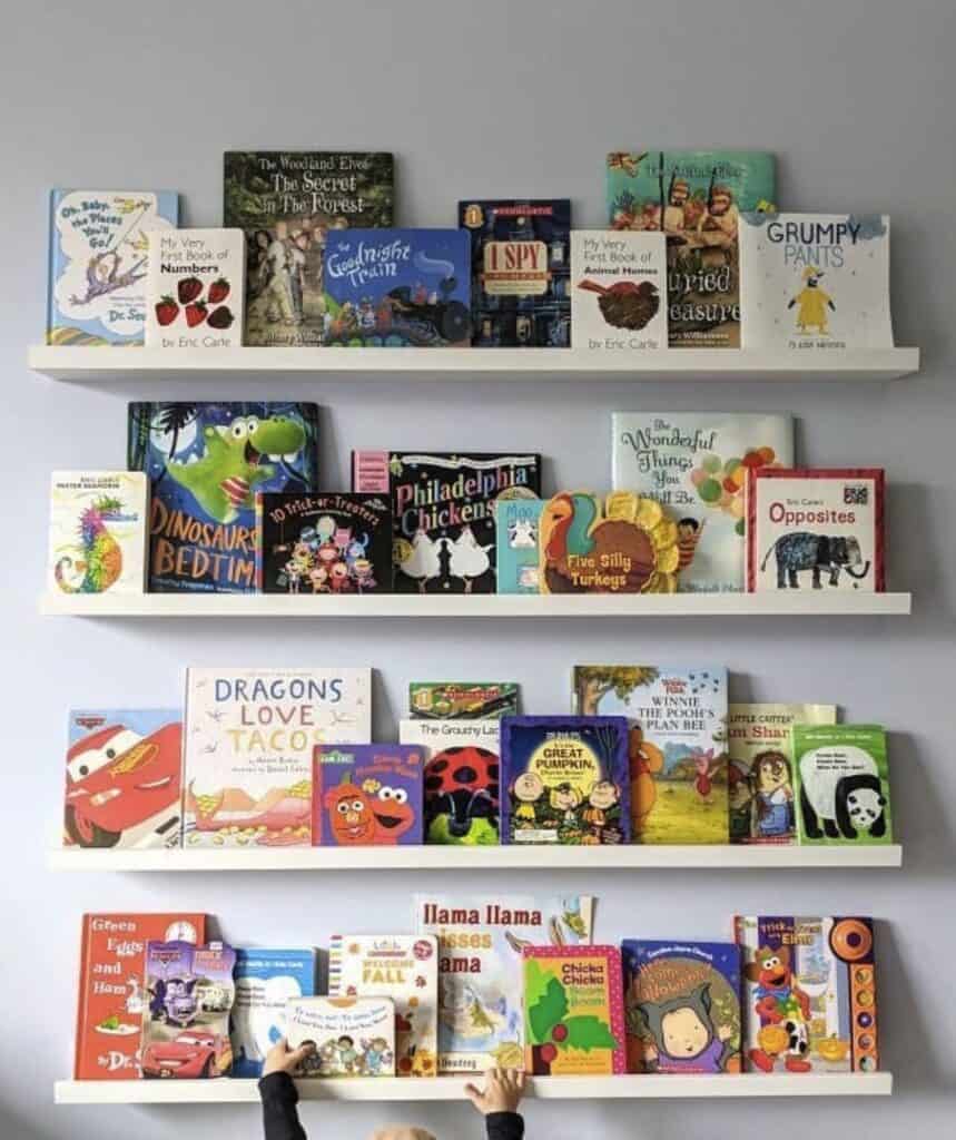Bright children's books arranged on white wall-mounted shelves at The Olive Branch Nest.