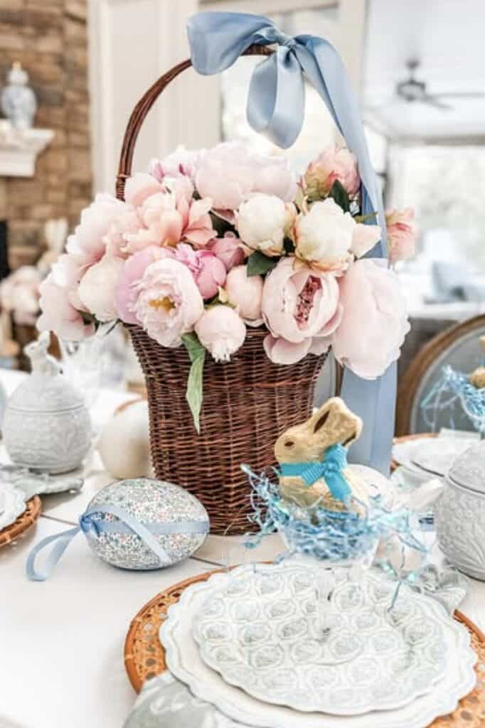 Beautiful pink peony flower arrangement in woven basket with blue ribbon, perfect for spring decor.