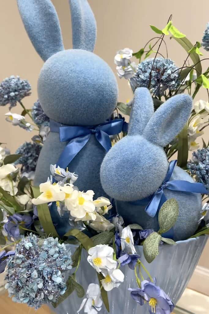 Decorative plush blue bunnies with ribbons in floral spring arrangement for Easter or seasonal decor.