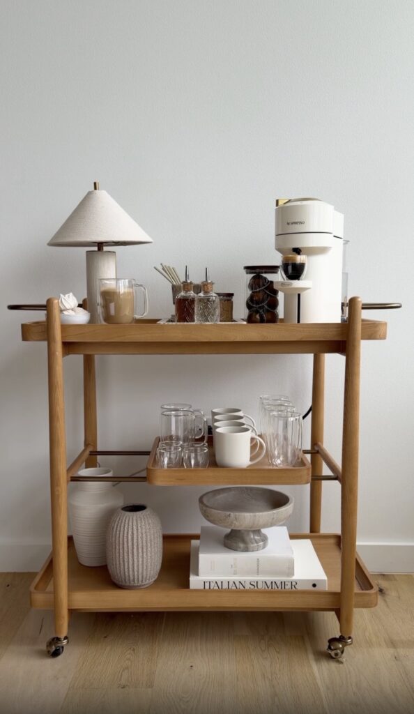 Wooden bar cart with glassware, coffee machine, and bar accessories for home bar setup.