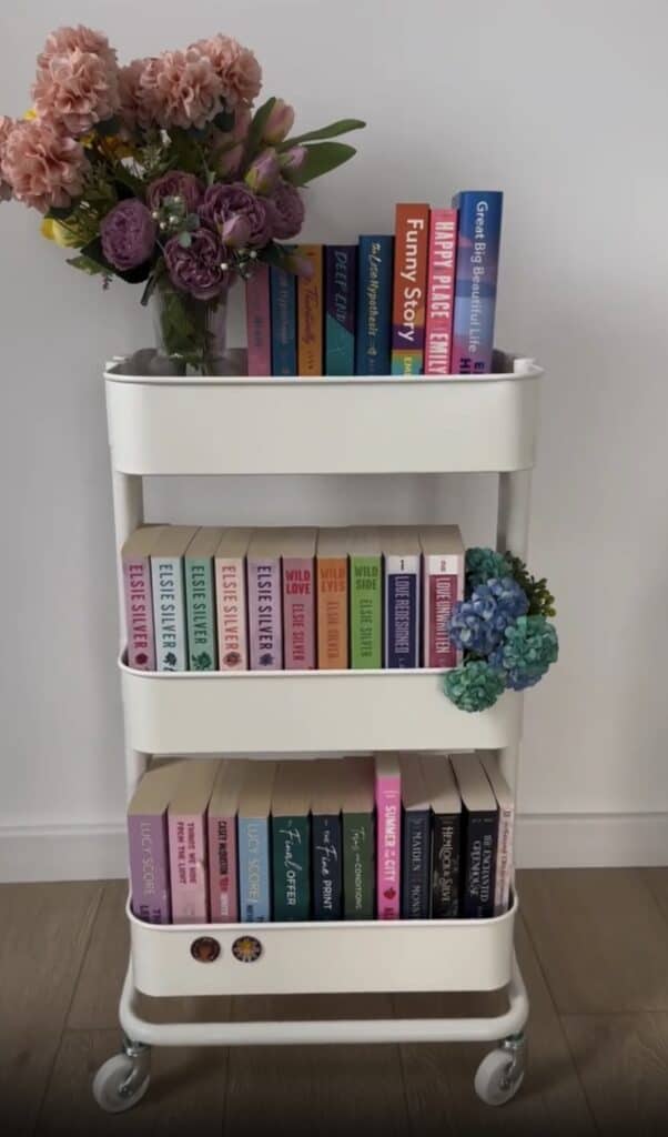 Stylish white bar cart featuring colorful books, pink and purple flowers, perfect for home entertain.