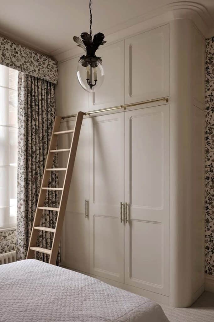 Built-in bedroom wardrobe with ladder and elegant decor.