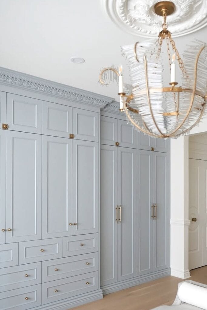 Spacious bedroom built-in closet with light blue cabinets and luxurious chandelier lighting.
