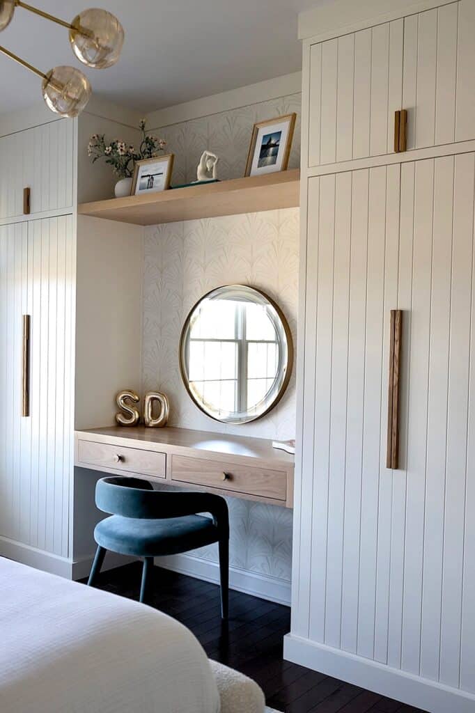 Modern built-in closet and vanity area with round mirror, decorative shelves, and cozy seating.