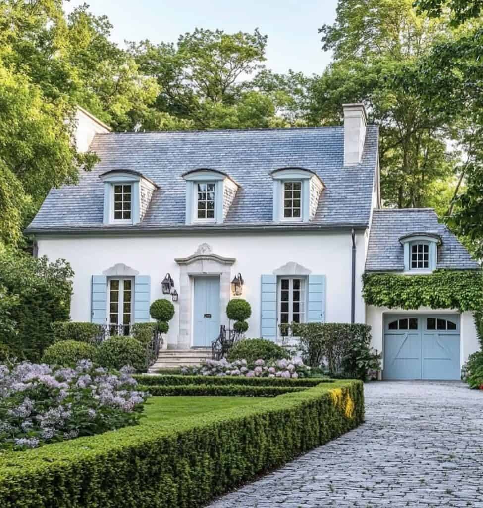 Elegant French country home with white facade, blue shutters, and lush garden.