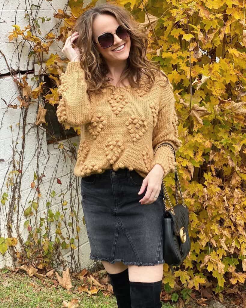 Woman wearing cozy sweater and short denim skirt outdoors.