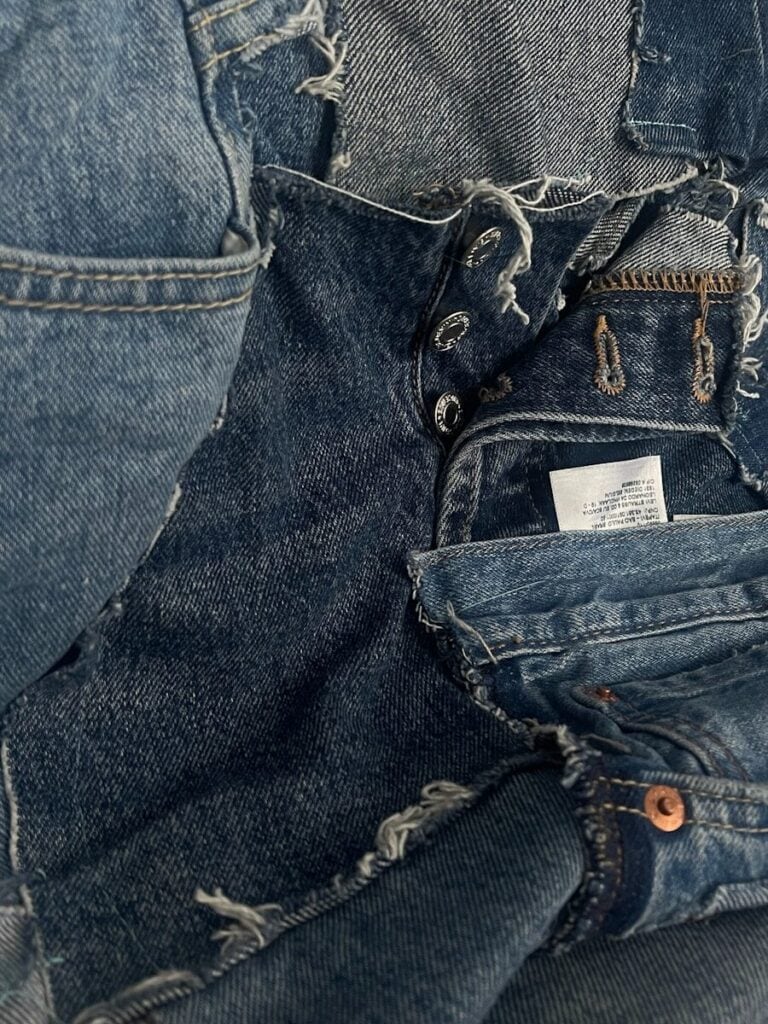 Close-up of distressed denim skirt with frayed edges and button details.