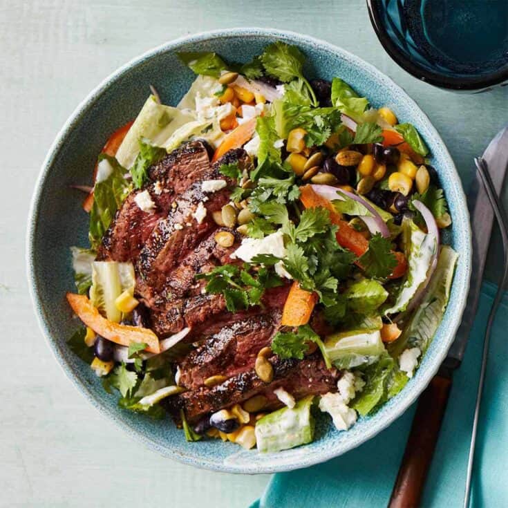 Healthy steak salad with mixed greens, corn, and fresh herbs in a blue bowl.