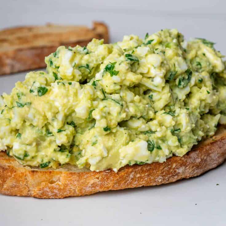 Creamy avocado egg salad on toasted bread with herbs and spices.