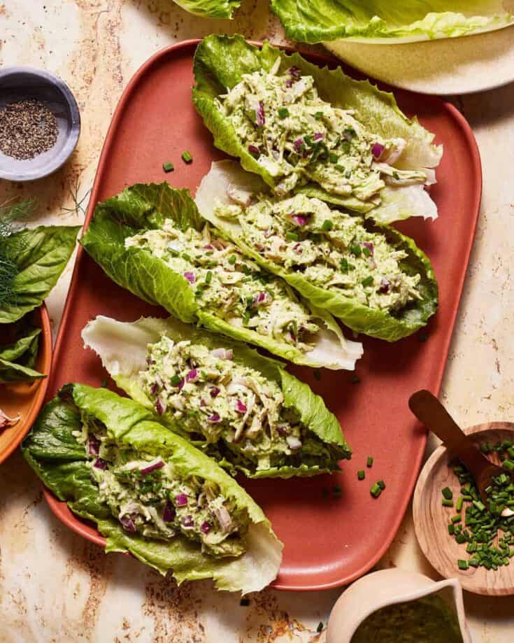 Fresh lettuce wraps filled with creamy avocado and chopped herbs on a pink plate.