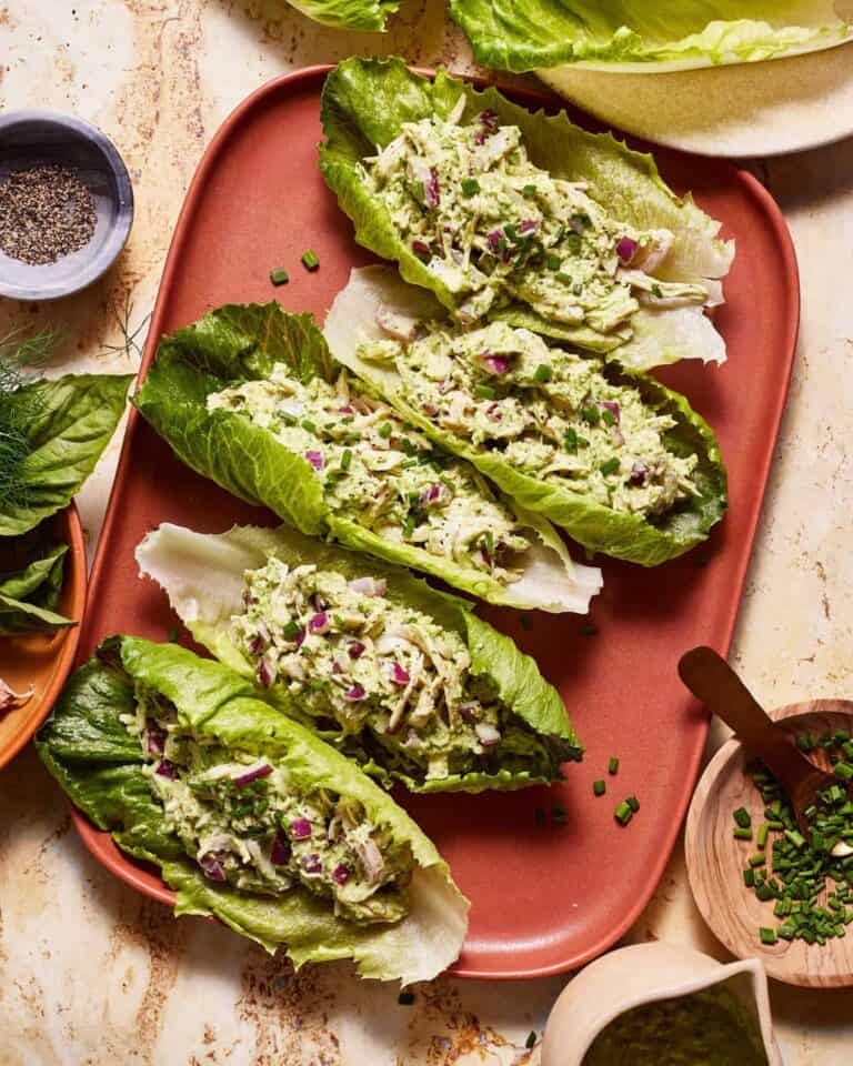Fresh lettuce wraps filled with creamy avocado and chopped herbs on a pink plate.