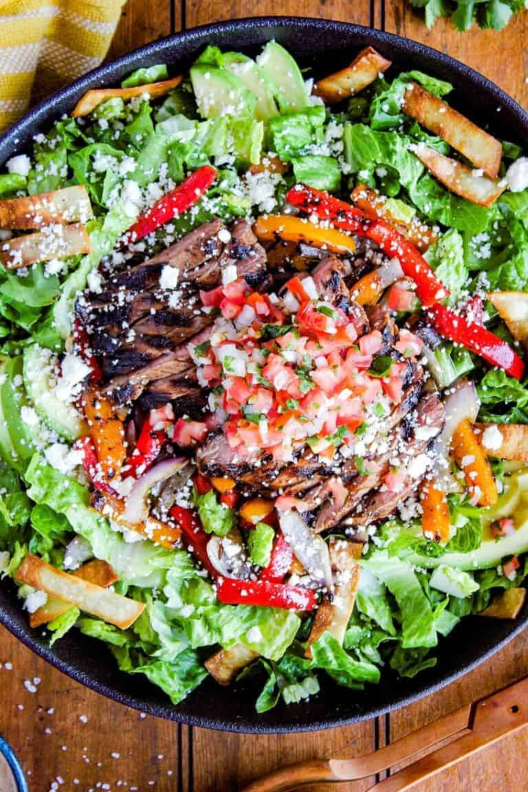 Colorful steak salad with vegetables, feta cheese, and salsa in a black bowl.