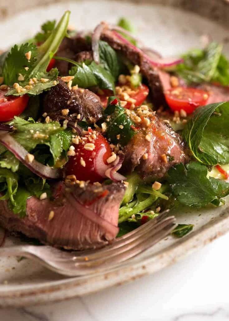 Healthy mixed green salad with tomatoes, herbs, and nuts on a ceramic plate.