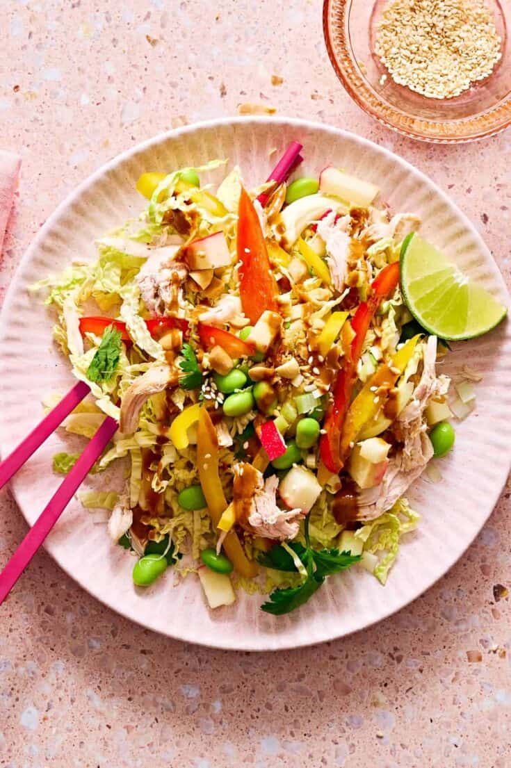 Colorful chicken salad with vegetables, lime wedge, and crunchy toppings on a white plate.