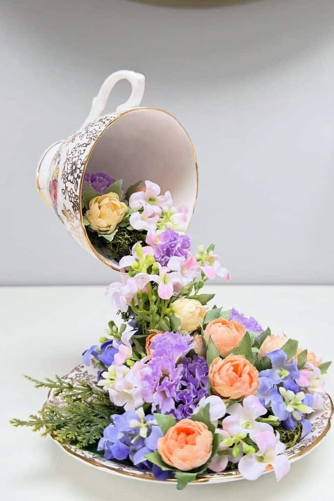 Beautiful floral display with roses, violets, and greenery flowing from a teacup onto a plate.