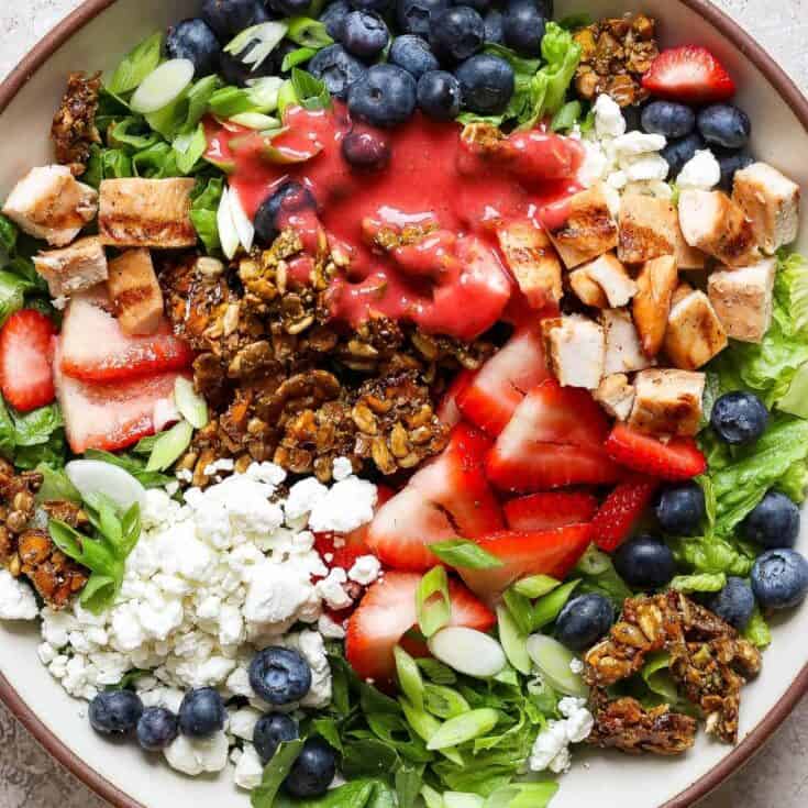Colorful salad with blueberries, strawberries, chicken, and greens in a bowl.