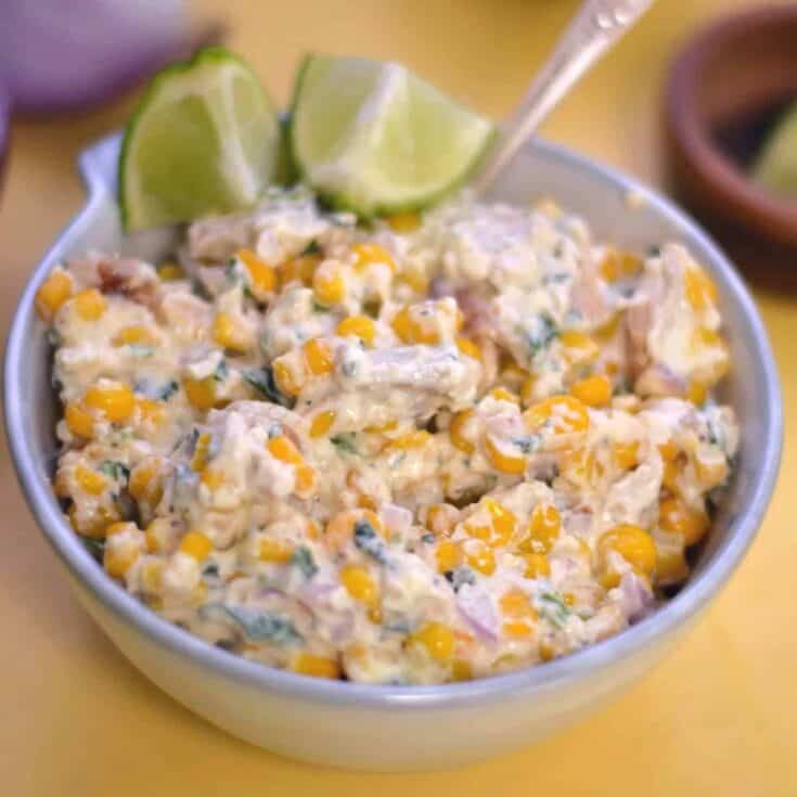 Delicious creamy corn and chicken salad garnished with lime wedges.