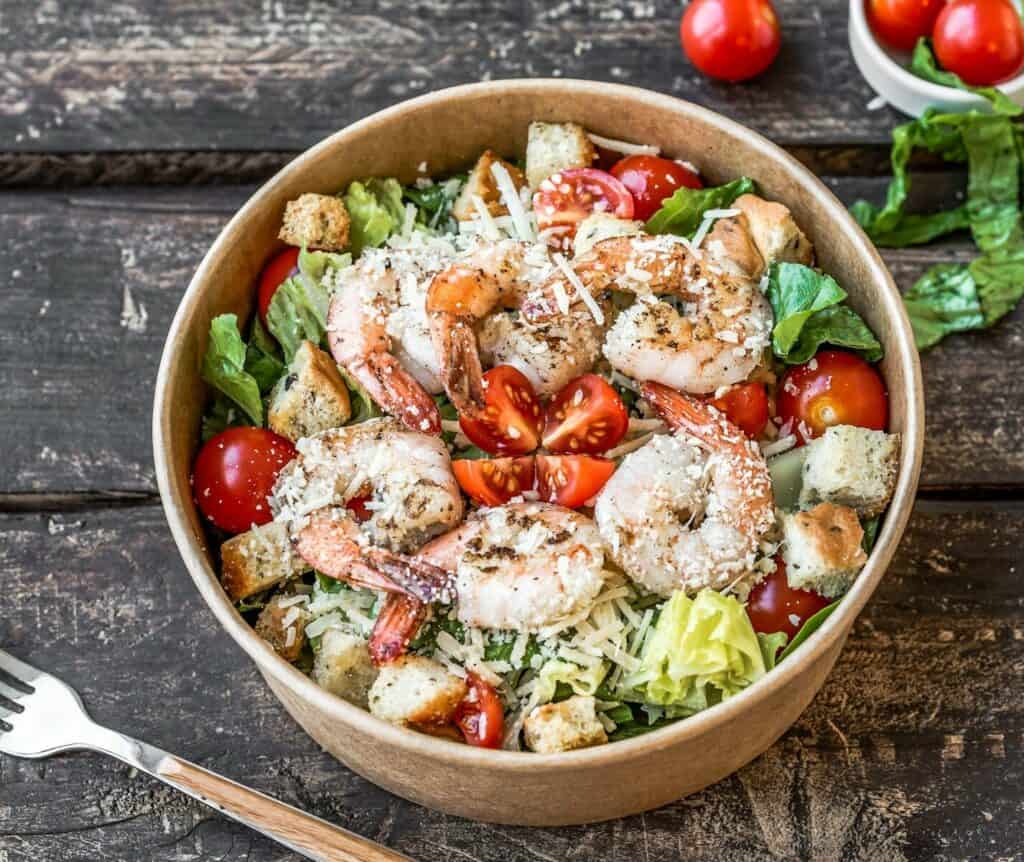 Healthy high-protein shrimp salad with cherry tomatoes, lettuce, croutons, and Parmesan cheese.
