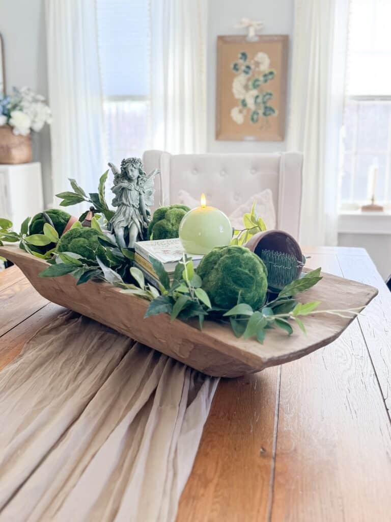 Decorative centerpiece with greenery, candle, and sculpture on dining table.