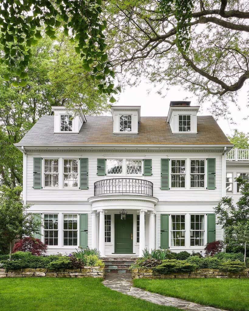 Beautiful white house with green shutters, surrounded by lush garden and mature trees.