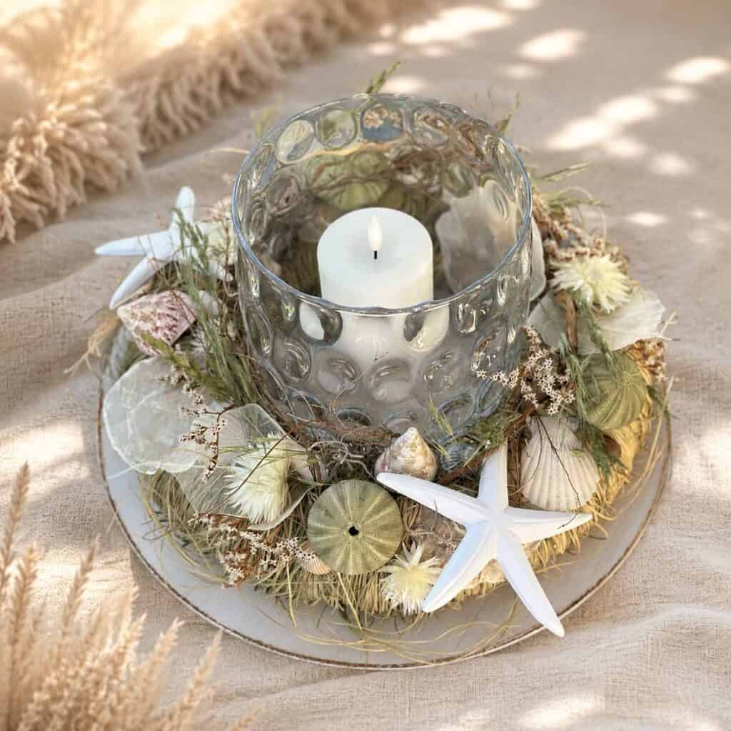 Decorative candle centerpiece with seashells and starfish for table decor.