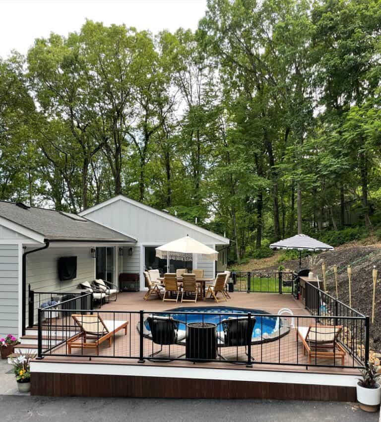 Outdoor pool and patio with seating, umbrellas, and lush green trees.